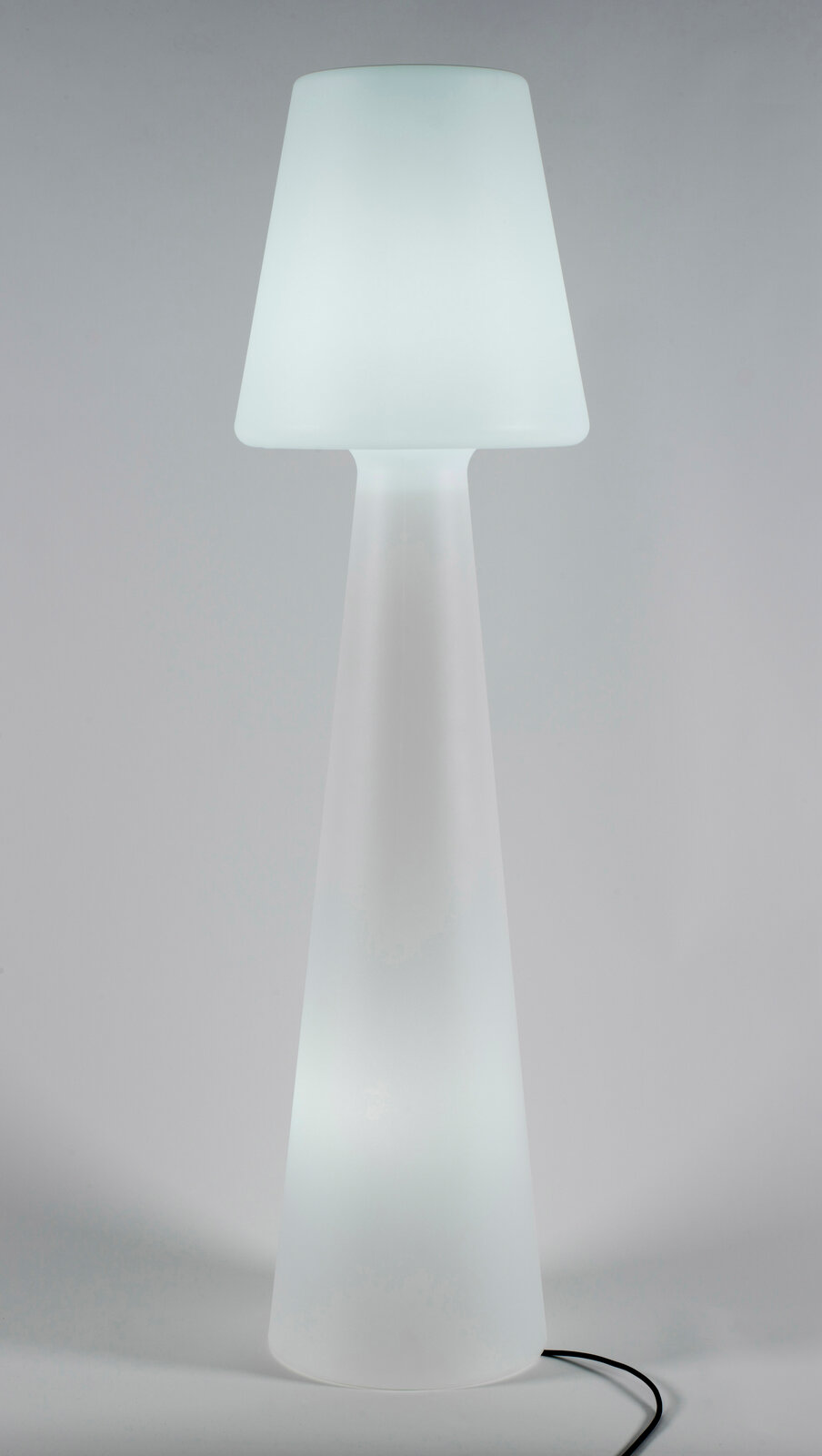 Weiße, leuchtende Stehlampe mit konischem Schirm und schlankem, konischem Fuß, Kabel sichtbar, frontal aus leicht erhöhter Perspektive vor grauem Hintergrund