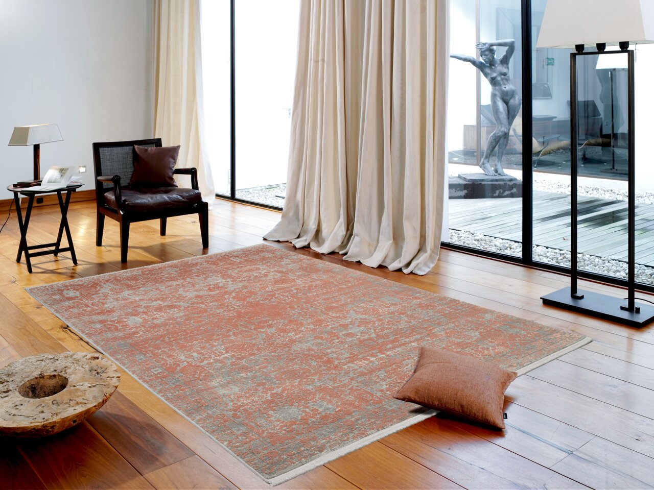 Designer Teppich in einem modernen Wohnzimmer mit Holzboden, einem Sessel, einem Beistelltisch und großen Fenstern. Perspektive von schräg oben.