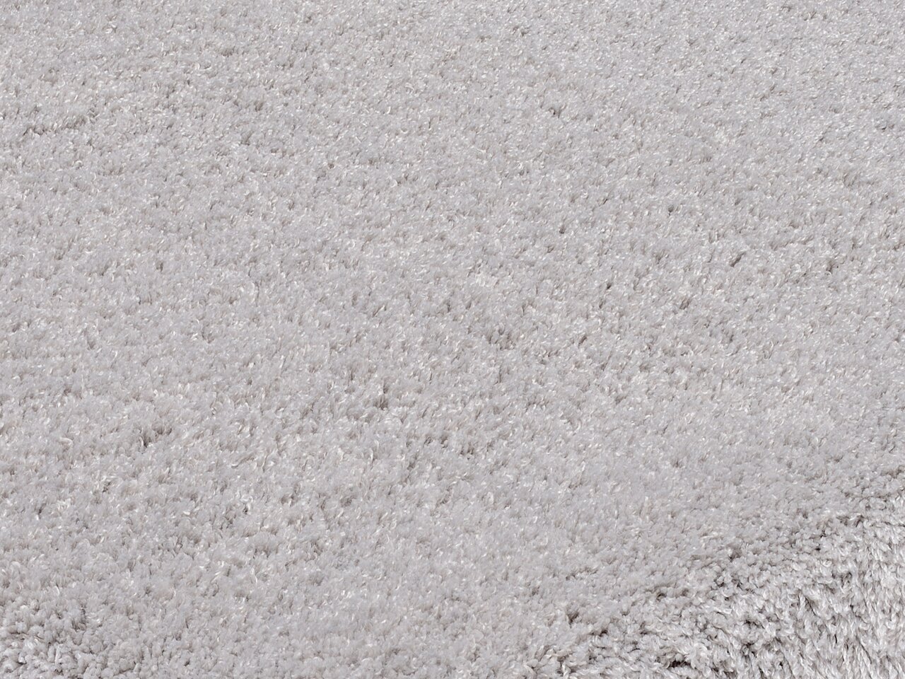 Nahaufnahme eines weichen, runden Teppichs in hellgrauer Farbe, perspektivisch von der Seite aufgenommen.