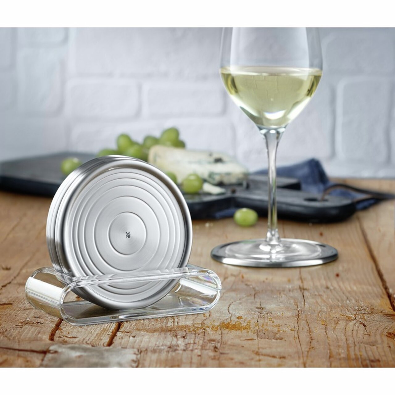 Silberne Gläserteller im modernen Design, präsentiert auf einem Holztisch mit einem Glas Weißwein und Käse im Hintergrund, seitliche Perspektive.