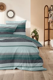 Bettwäsche-Set in Blau- und Grautönen mit Streifenmuster, auf einem Bett in einem gemütlichen Schlafzimmer mit Holzboden und Dekorationen, aus seitlicher Perspektive fotografiert.