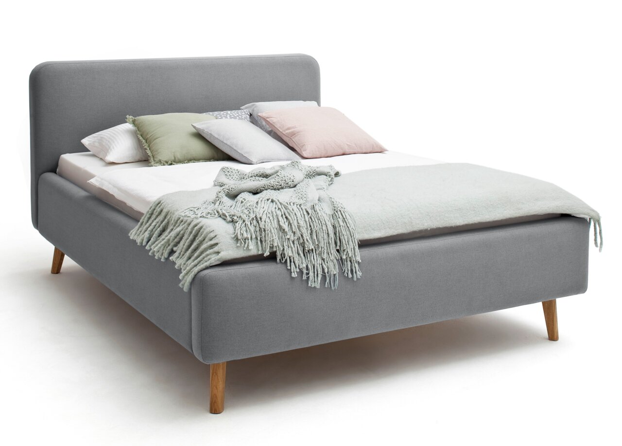 Graues Polsterbett mit Holzfüßen, dekoriert mit mehreren Kissen und einer Decke, seitliche Perspektive