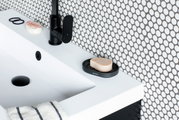 Zeepbakje van zwart materiaal met zeep, geplaatst op de rand van een witte wastafel, zijaanzicht