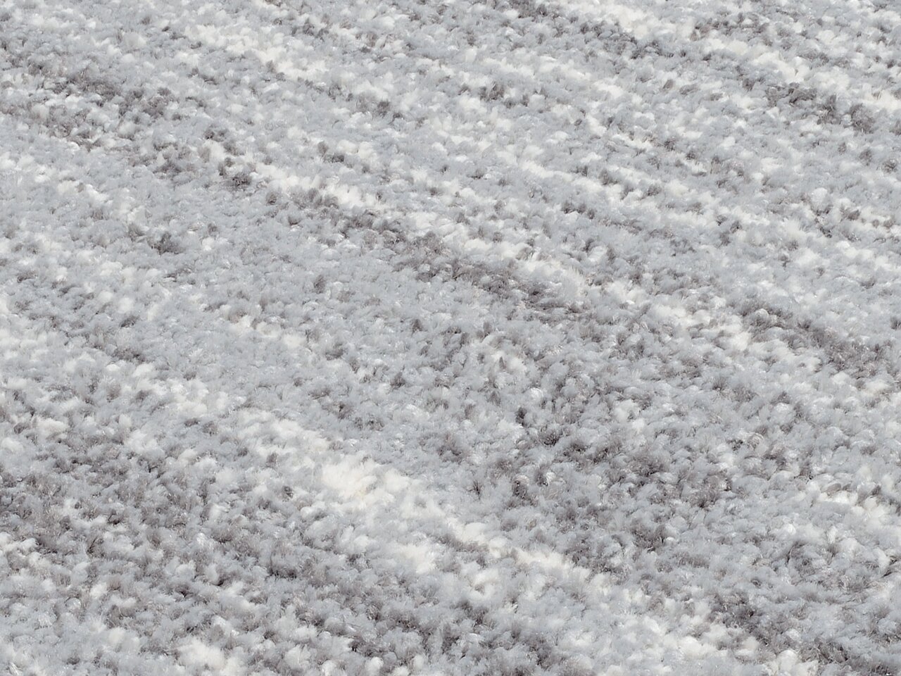 Nahaufnahme eines Uni-Teppichs in Grau- und Weißtönen mit flauschiger Textur, schräg von oben fotografiert.