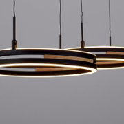 Close-up vanuit laag perspectief van moderne zwarte LED-hanglampen met ronde ringen, warme lichtlijnen en houten accenten.