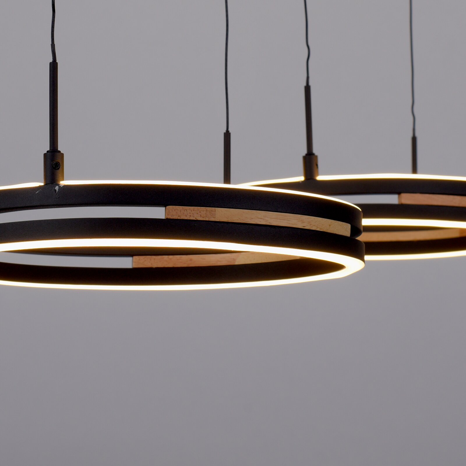 Close-up vanuit laag perspectief van moderne zwarte LED-hanglampen met ronde ringen, warme lichtlijnen en houten accenten.