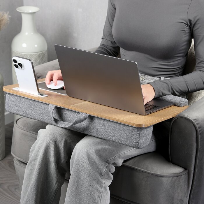Houten laptopkussen met grijze stoffen onderkant en draaggreep, met laptop en smartphonehouder in gebruik op schoot; gefotografeerd schuin van voren op zithoogte.