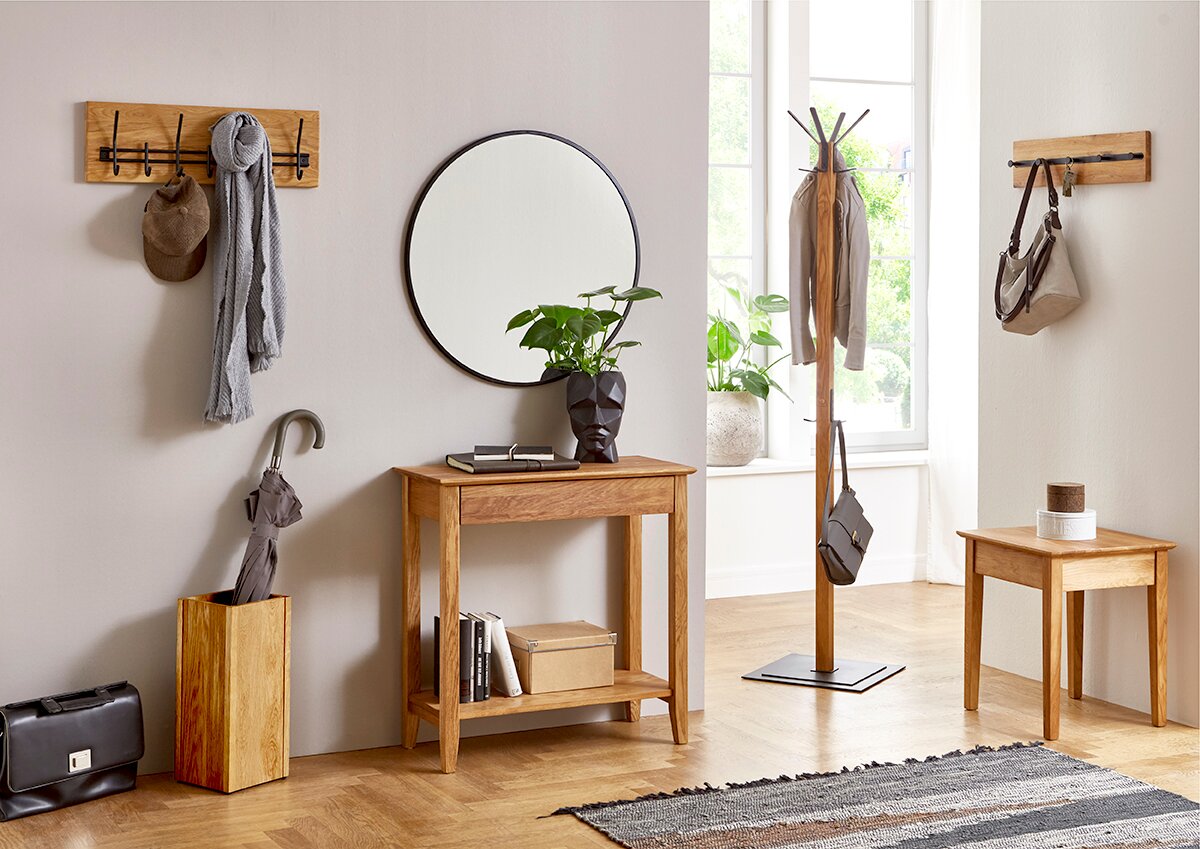 Heller Flur mit Eichenholz-Konsolentisch und rundem Wandspiegel, links Wandgarderobe mit Schal und Cap sowie Schirmständer, rechts freistehender Garderobenständer und kleiner Beistelltisch – Frontansicht auf Augenhöhe.