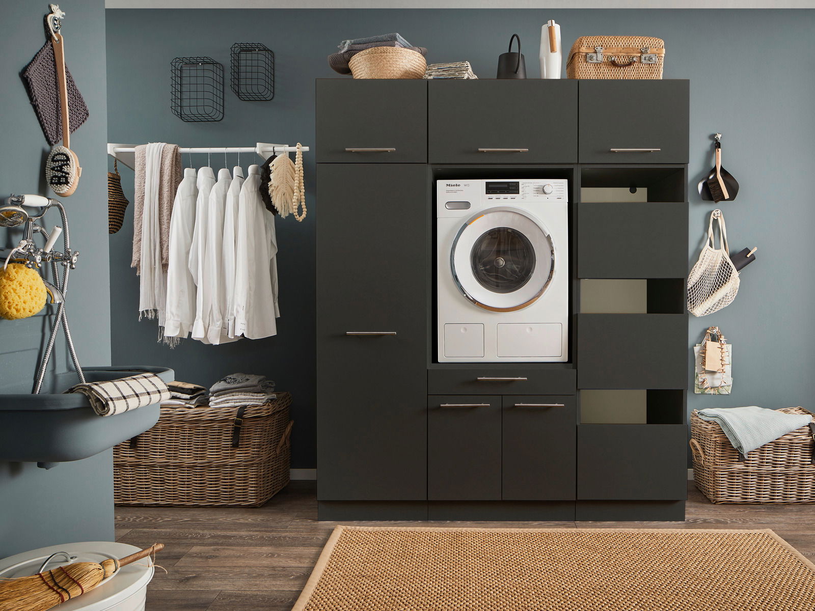 XORA Wäscheschrank PRIMUS Moderne Waschküche mit dunklem Hochschrank, integriertem Waschgerät und offenen Schubladen, frontal betrachtet.