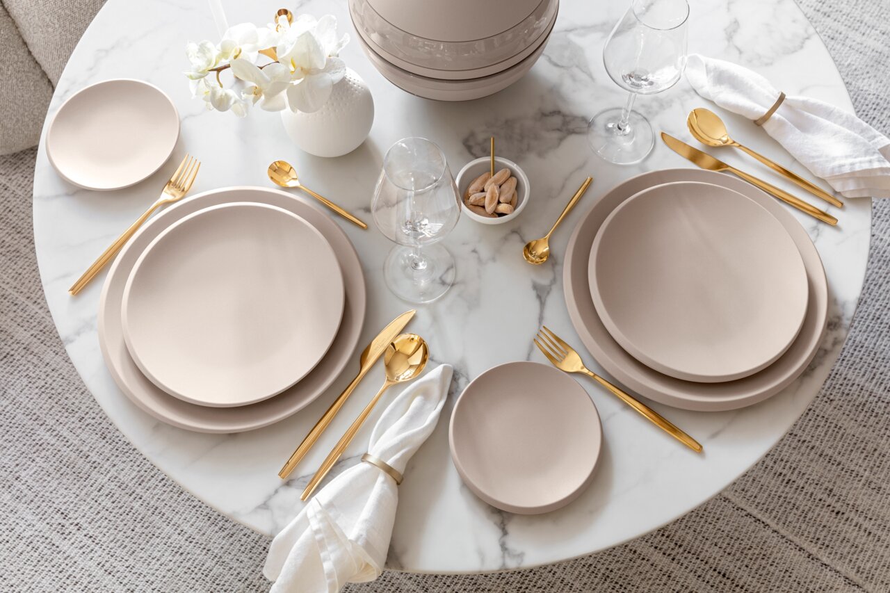 Villeroy & Boch Speiseteller NewMoon 27cm bei. NEW MOON Elegante Tischdekoration mit Speisetellern NewMoon 27cm, goldfarbenem Besteck und weißen Servietten auf einem runden Marmortisch, Vogelperspektive.