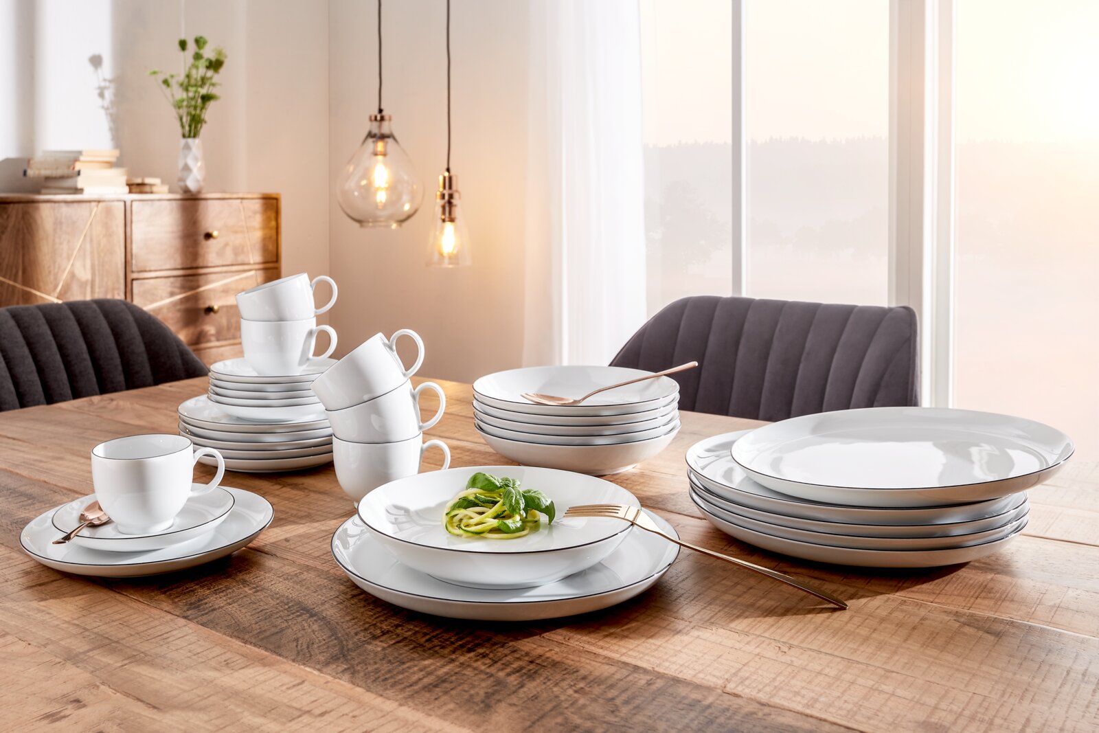 Elegantes Kombiservice Lido Black 30-teilig auf einem Holztisch, mit Tellern, Tassen und Schalen in einem modernen Esszimmer, seitliche Perspektive.