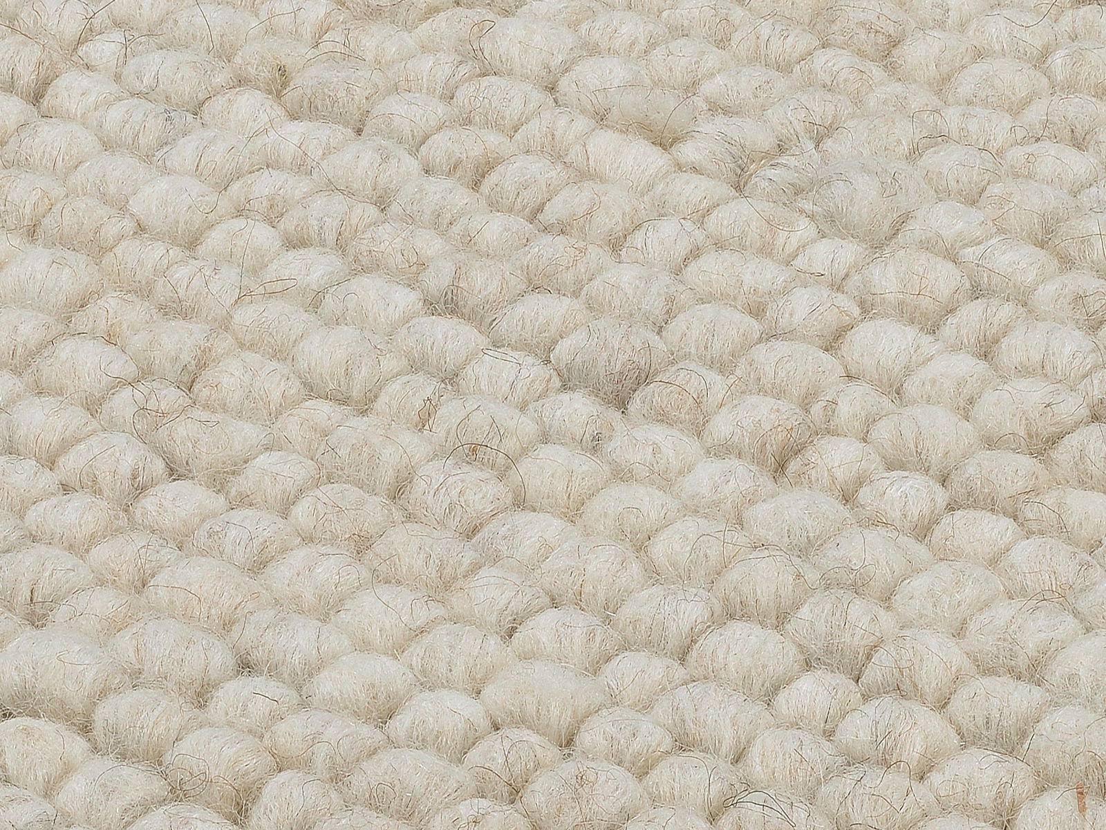 Nahaufnahme eines handgewebten Teppichs mit grober, wolliger Struktur in cremeweißer Farbe, von oben betrachtet.