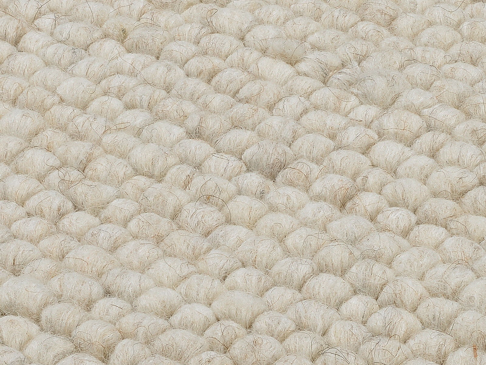 Nahaufnahme eines handgewebten Teppichs mit grober, wolliger Struktur in cremeweißer Farbe, von oben betrachtet.