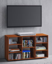 Holzfarbenes TV-Lowboard/Medienregal mit mehreren offenen Fächern, gefüllt mit DVDs und CDs, mit einem weißen DVD-Player obenauf; frontale Ansicht leicht von links vor Betonwand mit darüber montiertem Flachbildfernseher.