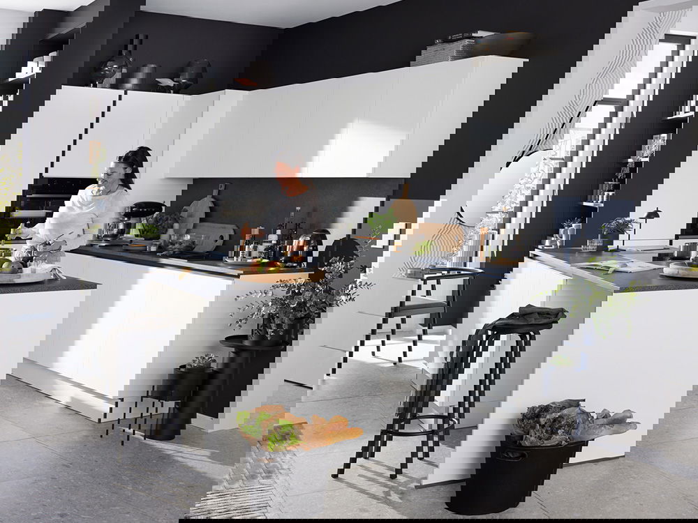 Moderne Küche in grau-weiß mit Kochinsel, großen Fenstern und stilvoller Einrichtung, ein Paar bereitet Essen zu.