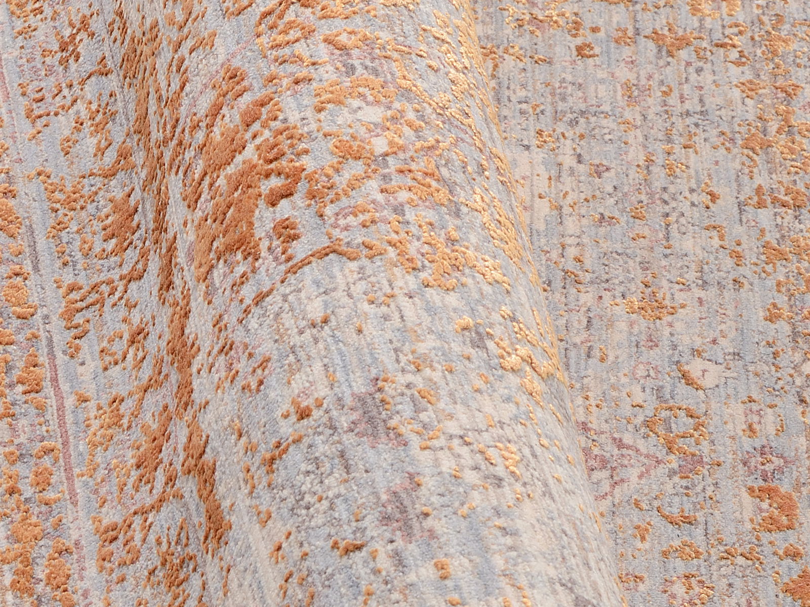 Nahaufnahme eines Designer-Teppichs mit abstraktem Muster in Orange- und Grautönen, perspektivisch von der Seite aufgenommen.