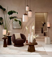 Stilvolles Wohnzimmer-Arrangement mit drei zylindrischen Pendelleuchten aus hellem Schirm und dunklem Holz, braunem Sessel, Holztischen, weißen Vasen und Pflanzen, frontal aus leicht erhöhter Perspektive.