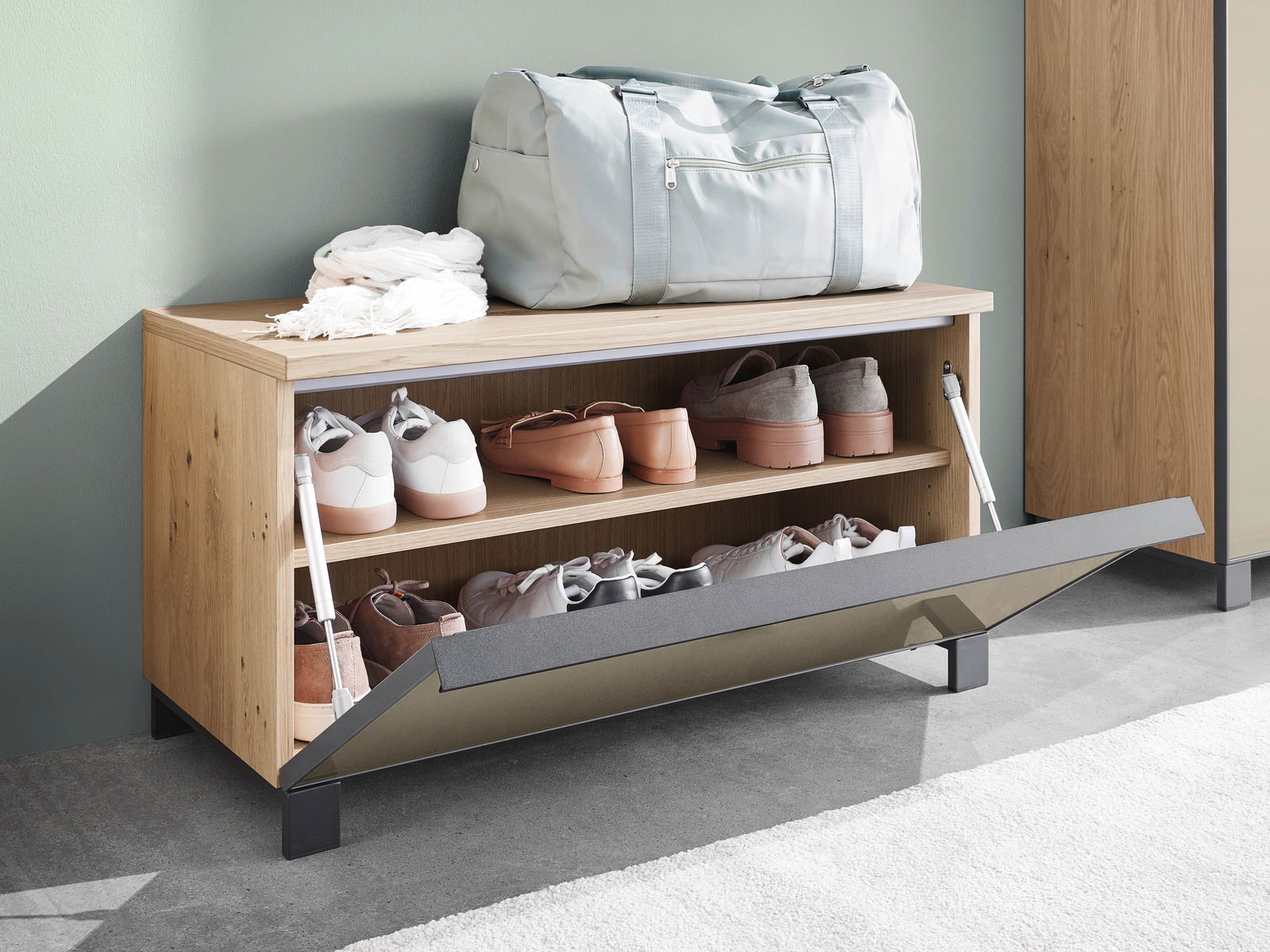 Garderobenbank aus Holz mit Schuhablage, darauf eine Sporttasche und ein Schal, seitliche Perspektive