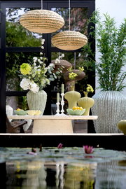 Ein stilvoller Kerzenständer auf einem Tisch, umgeben von grünen Vasen und Blumen, mit einer modernen, natürlichen Atmosphäre. Perspektive von vorne.