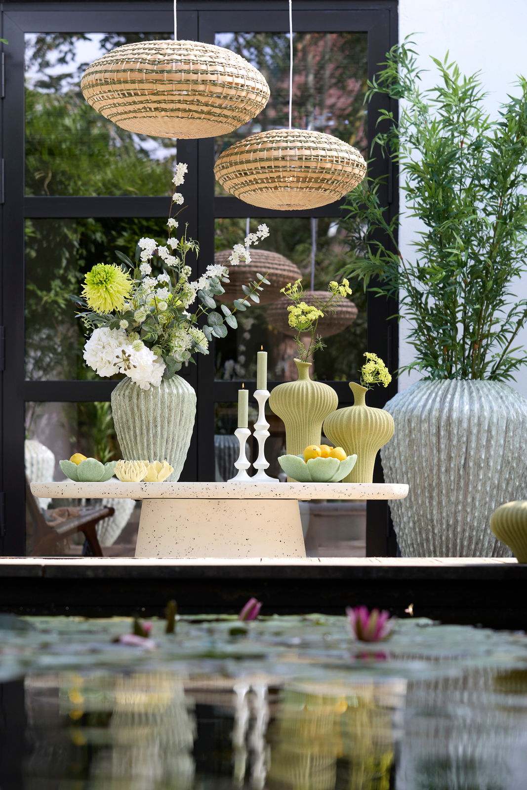 Ein stilvoller Kerzenständer auf einem Tisch, umgeben von grünen Vasen und Blumen, mit einer modernen, natürlichen Atmosphäre. Perspektive von vorne.