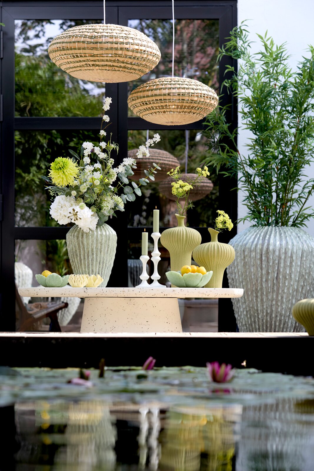 Light&Living Kerzenständer ISARA Ein stilvoller Kerzenständer auf einem Tisch, umgeben von grünen Vasen und Blumen, mit einer modernen, natürlichen Atmosphäre. Perspektive von vorne.