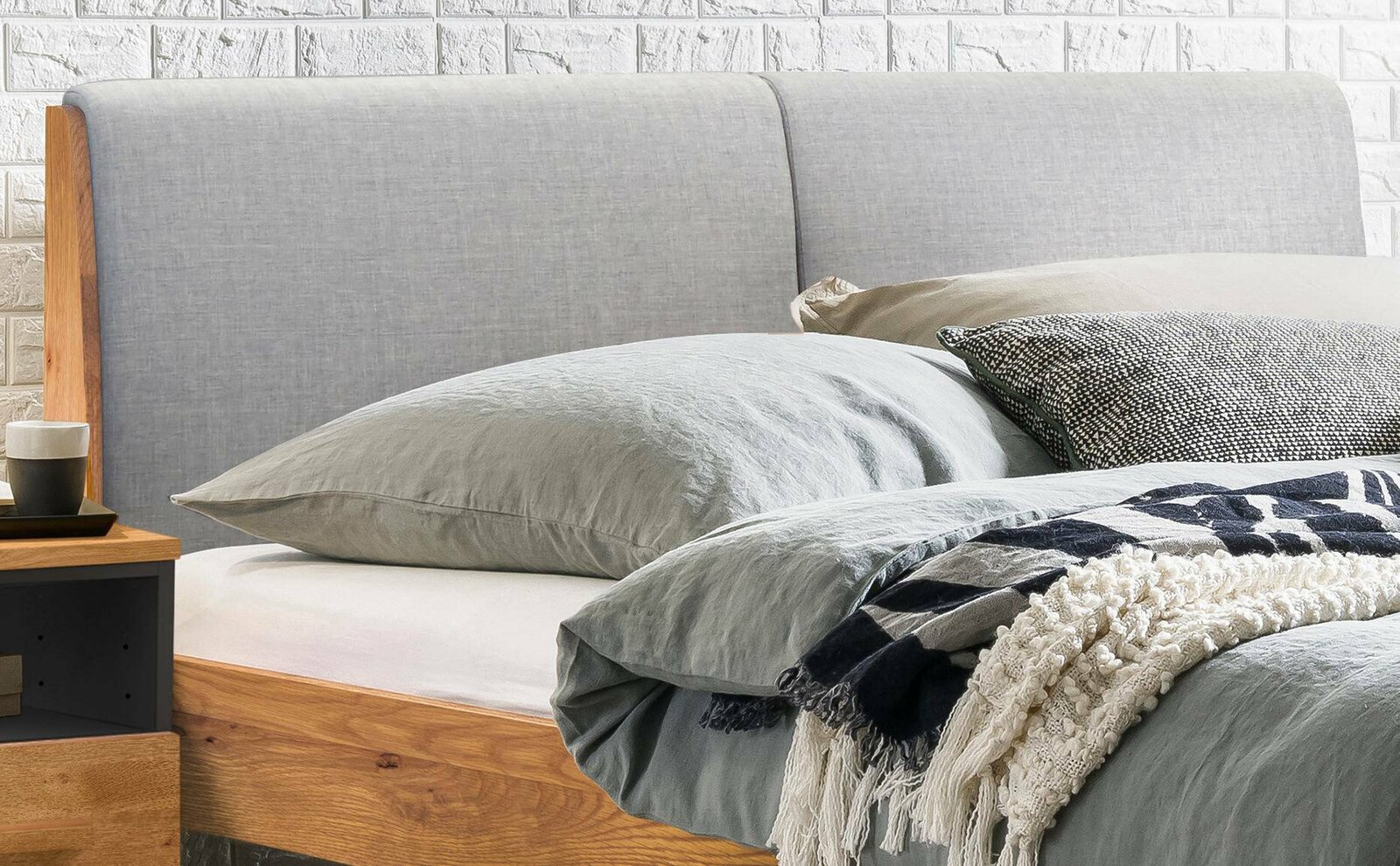 Nahaufnahme eines Bettgestells mit grauem Kopfteil und Holzelementen, seitliche Perspektive