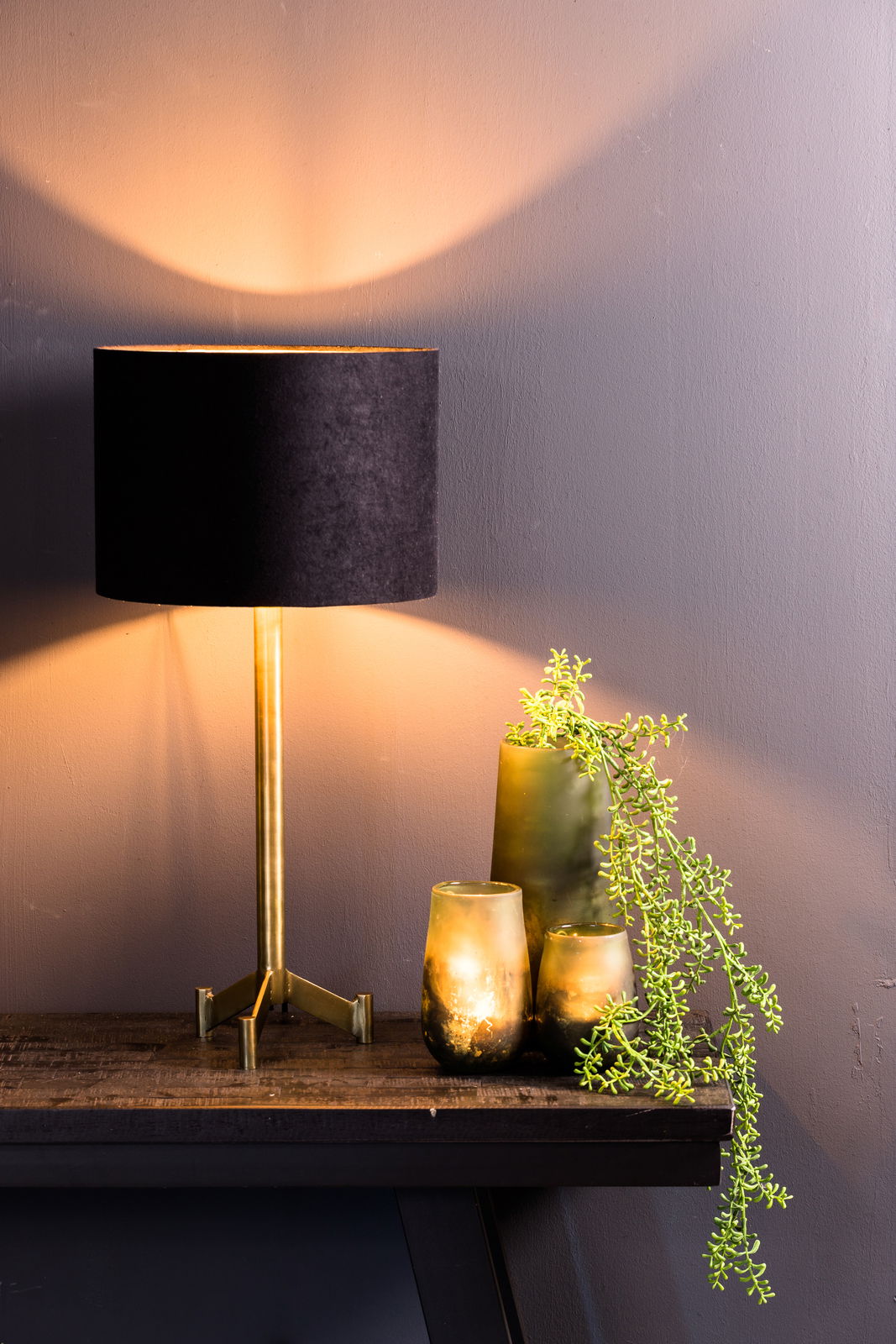 Schwarzer Lampenschirm auf einem goldenen Ständer, seitliche Perspektive, mit warmem Lichtschein an der Wand.
