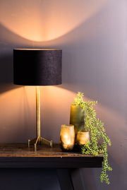 Schwarzer Lampenschirm auf einem goldenen Ständer, seitliche Perspektive, mit warmem Lichtschein an der Wand.