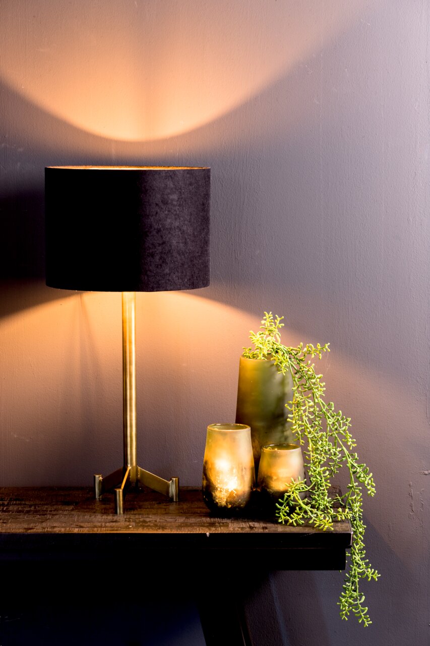 Schwarzer Lampenschirm auf einem goldenen Ständer, seitliche Perspektive, mit warmem Lichtschein an der Wand.