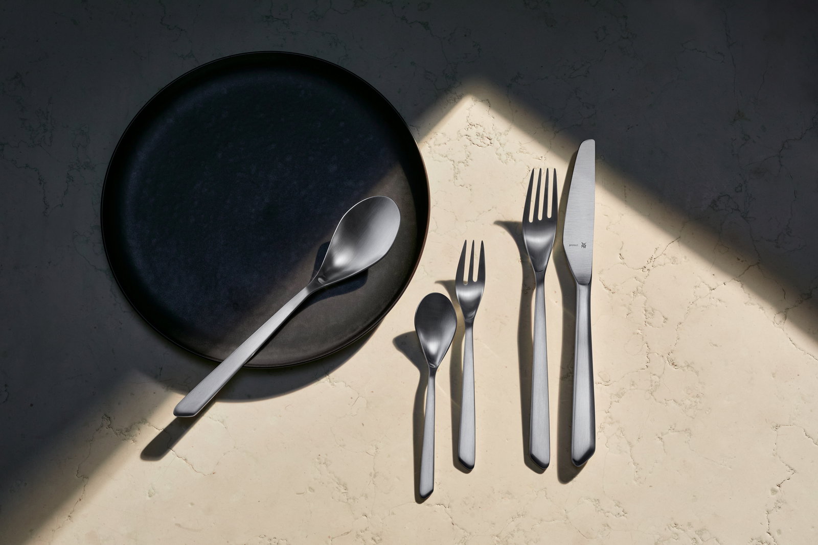 Besteckset Neo 30-tlg. aus Edelstahl, bestehend aus Messer, Gabel, Löffel und Teelöffel, auf einem hellen Marmortisch von oben fotografiert.