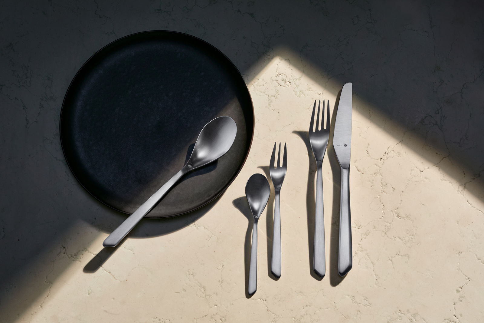 Besteckset Neo 30-tlg. aus Edelstahl, bestehend aus Messer, Gabel, Löffel und Teelöffel, auf einem hellen Marmortisch von oben fotografiert.