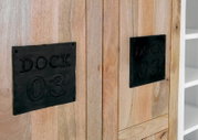 Nahaufnahme eines Highboards aus Holz mit schwarzen Metallplatten, die mit 'DOCK 03' beschriftet sind. Perspektive von vorne.