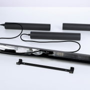 Schwarze lineare LED-Leuchte mit Anschlusskabel, LED-Treiber und Montagehalterung, schräg von oben in Seitenansicht auf weißem Hintergrund