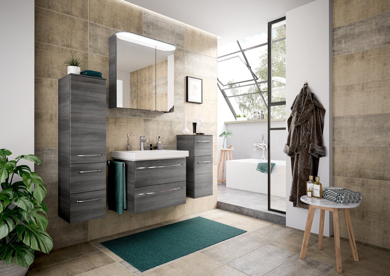 Moderne Badezimmermöbel in grauer Holzoptik, bestehend aus einem Waschtisch mit Spiegel und Schränken, in einer stilvollen Badezimmerumgebung mit Blick auf eine Badewanne und große Fenster.
