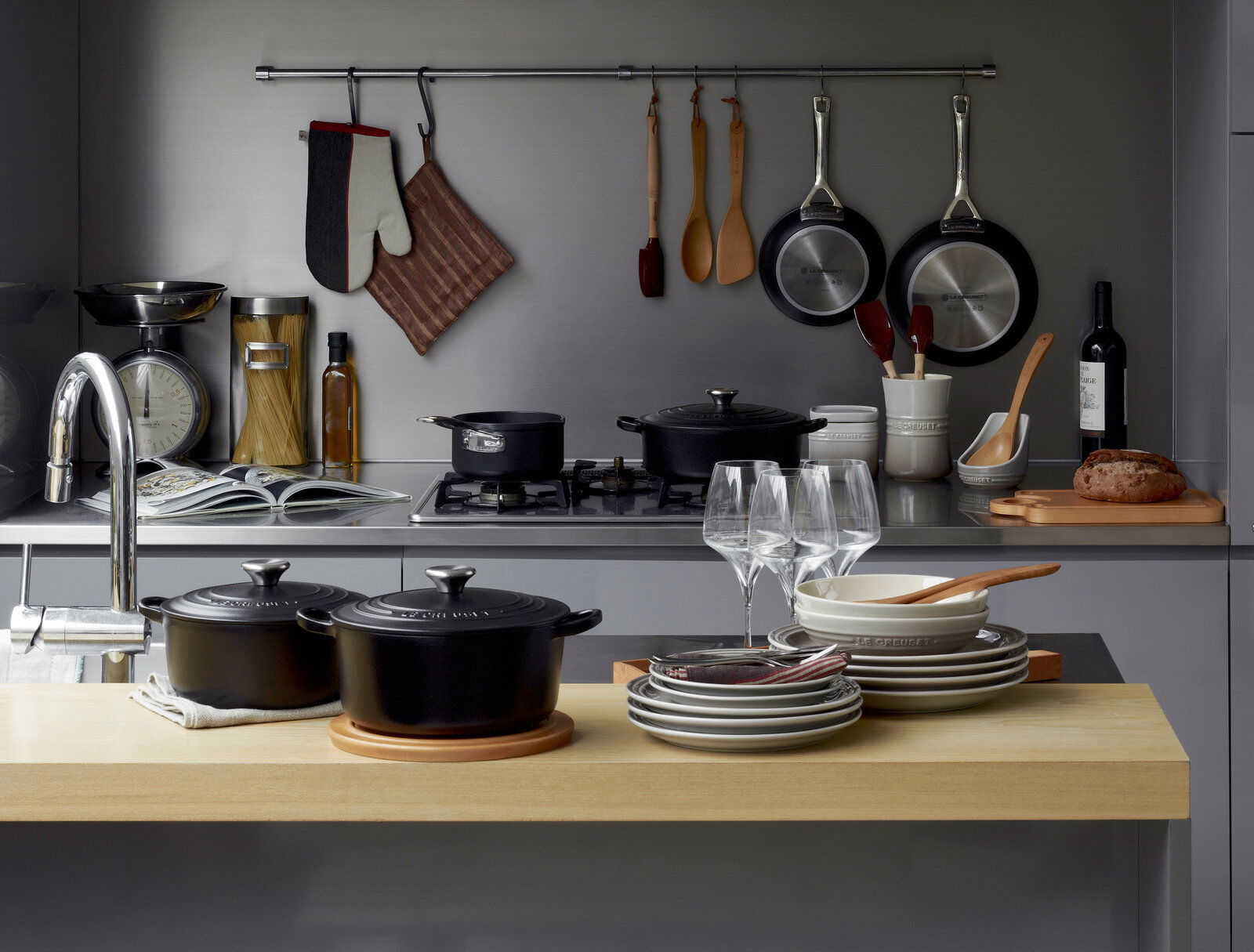 LE CREUSET Ronde braadpan 24 cm, zwart SIGNATURE Schwarzer runder Bräter mit Deckel, 24 cm, in einer modernen Küche auf einem Holzarbeitsplatz, umgeben von Geschirr und Küchenutensilien, aus der Vogelperspektive.
