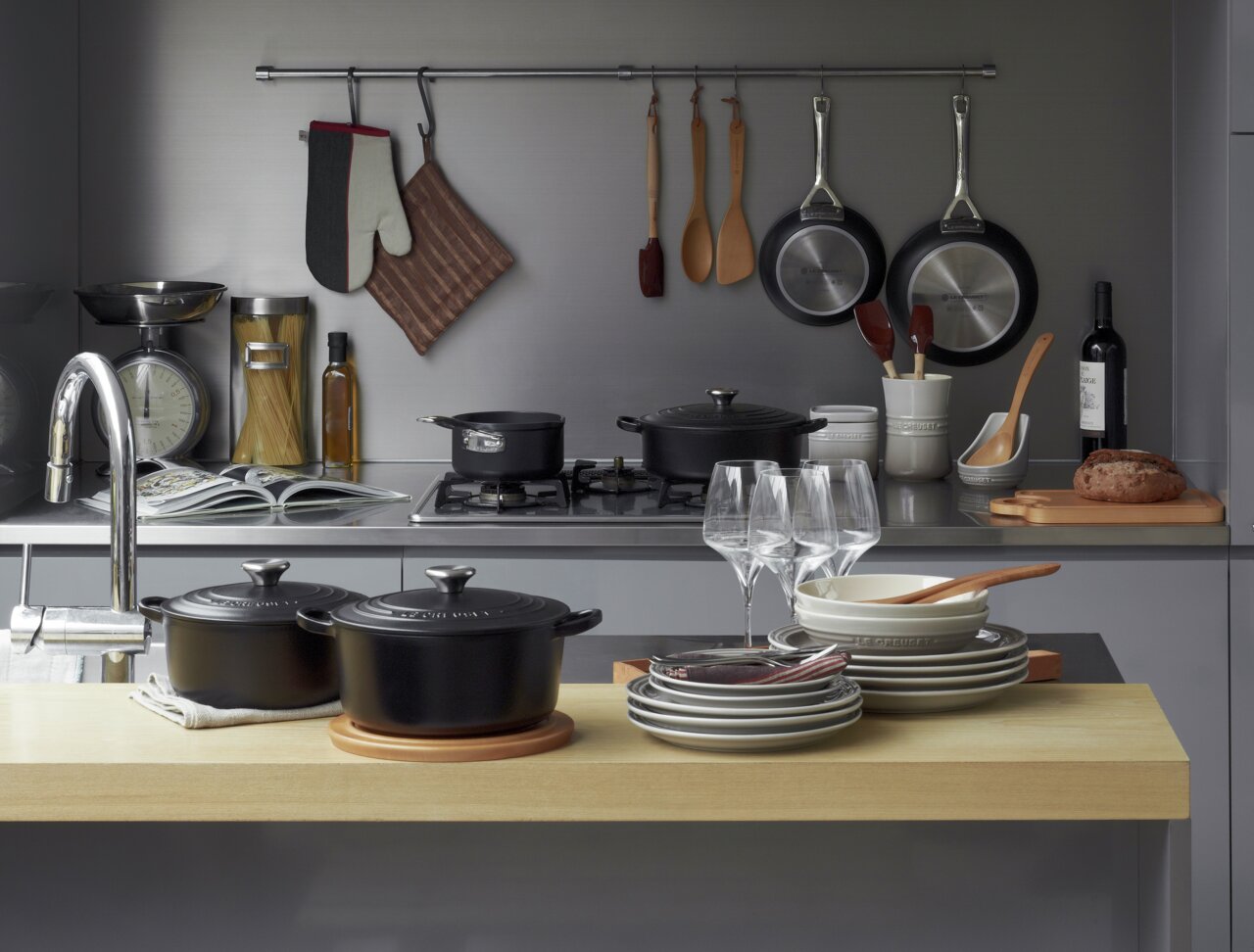 Zwarte ronde braadpan met deksel, 24 cm, in een moderne keuken op een houten werkblad, omringd door serviesgoed en keukengerei, gezien vanuit vogelperspectief.