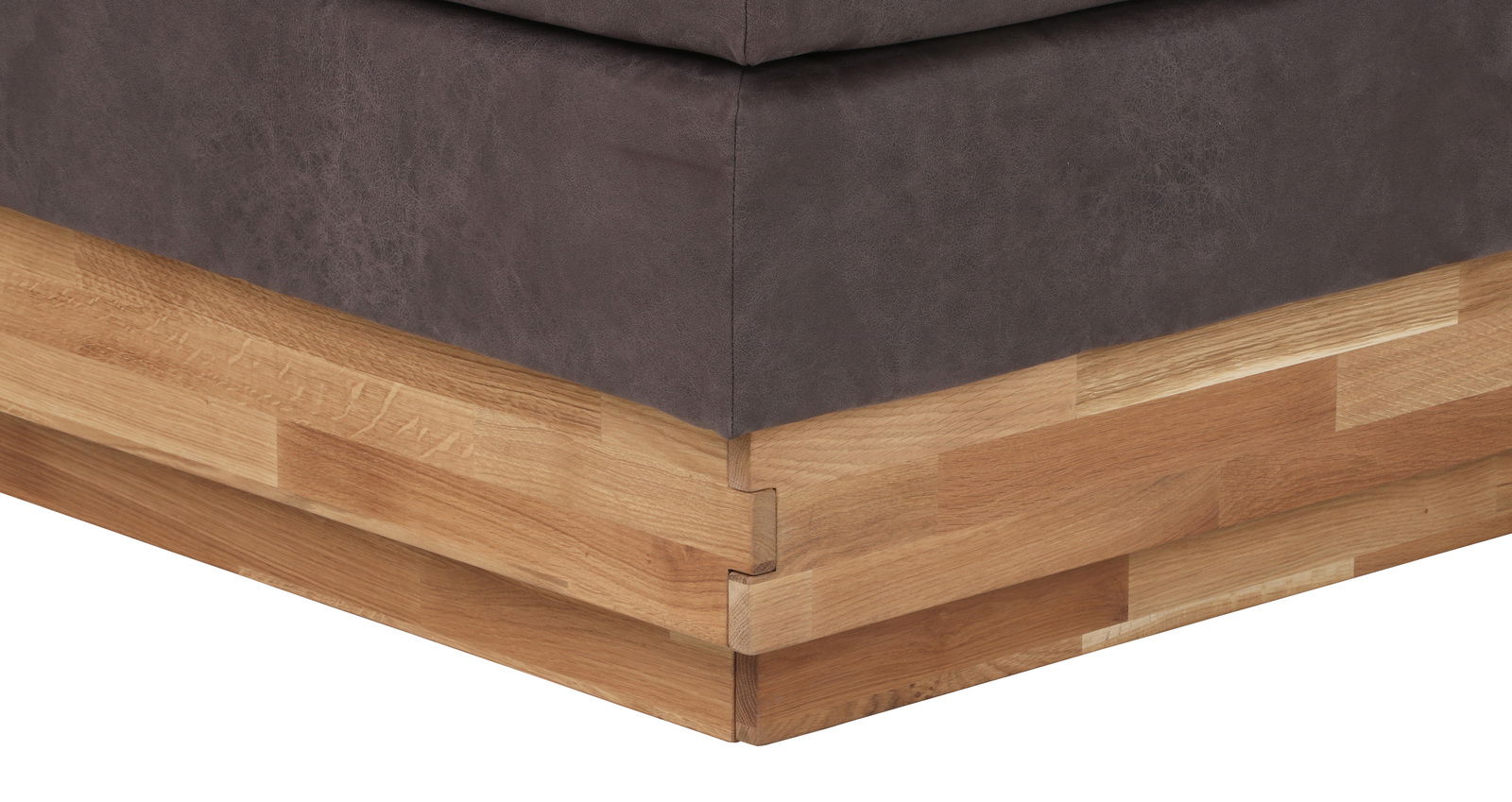 Nahaufnahme der Ecke eines Boxspringbetts mit grauem Stoffbezug und Holzunterbau, Perspektive von unten.