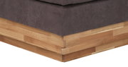 Nahaufnahme der Ecke eines Boxspringbetts mit grauem Stoffbezug und Holzunterbau, Perspektive von unten.