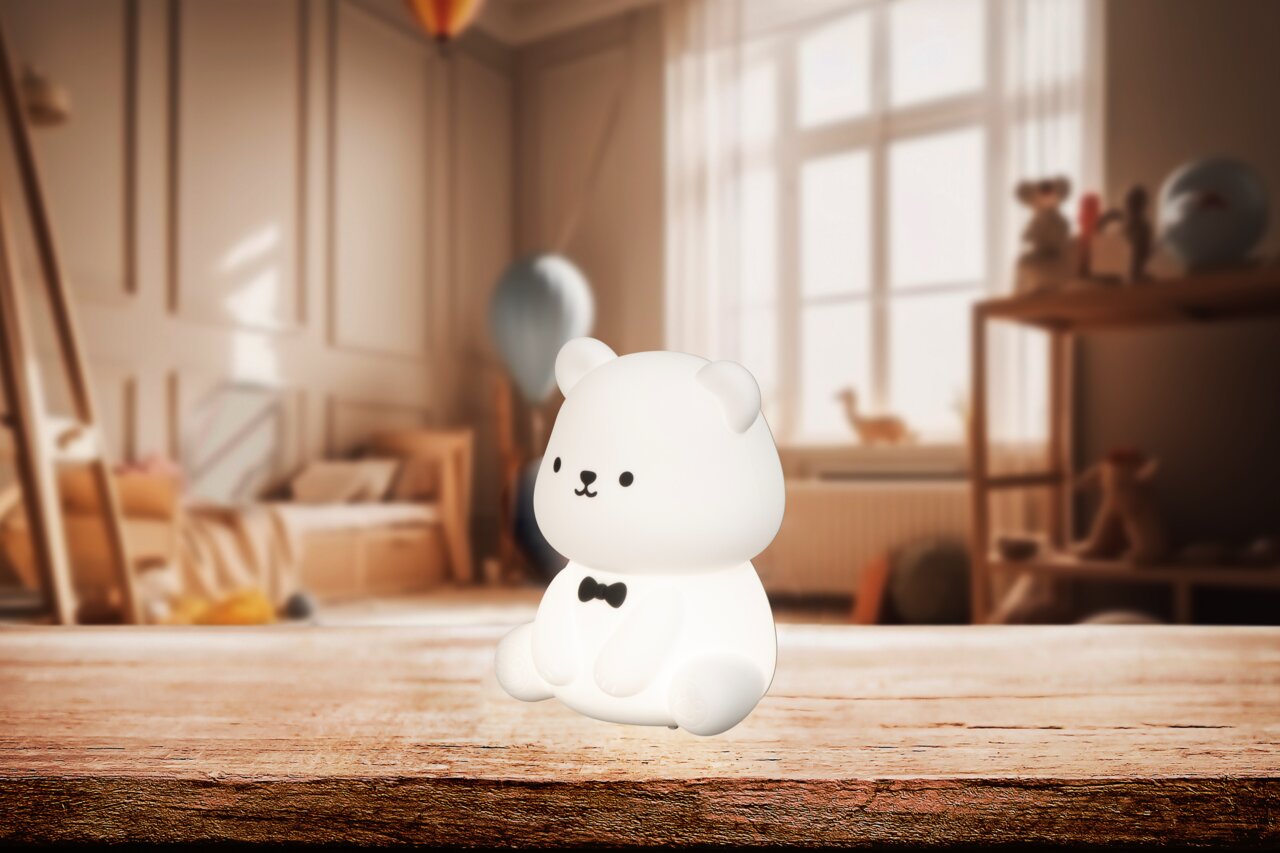 FHL easy Akku-Nachtlicht Bear KARL Niedliches Akku-Nachtlicht in Bärenform mit schwarzer Fliege, auf einem Holztisch in einem gemütlichen Kinderzimmer platziert, seitliche Perspektive.