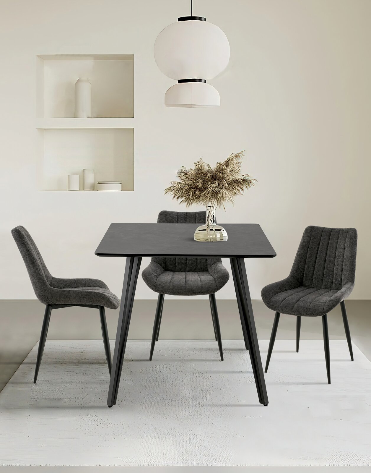 Moderner Esstisch mit schwarzer Tischplatte und vier grauen Stühlen, frontal betrachtet. Über dem Tisch hängt eine stilvolle weiße Lampe, und auf dem Tisch steht eine Vase mit getrockneten Gräsern.