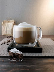 Cappuccinoglas mit Henkel, gefüllt mit Cappuccino und Milchschaum, auf einem Tablett, seitliche Perspektive