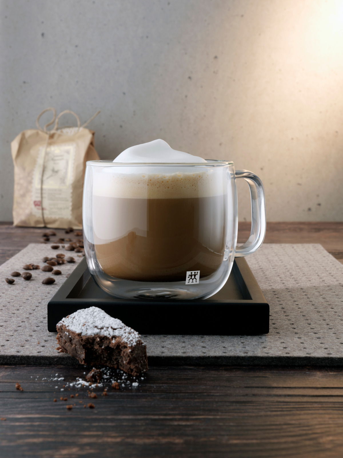 Cappuccinoglas mit Henkel, gefüllt mit Cappuccino und Milchschaum, auf einem Tablett, seitliche Perspektive