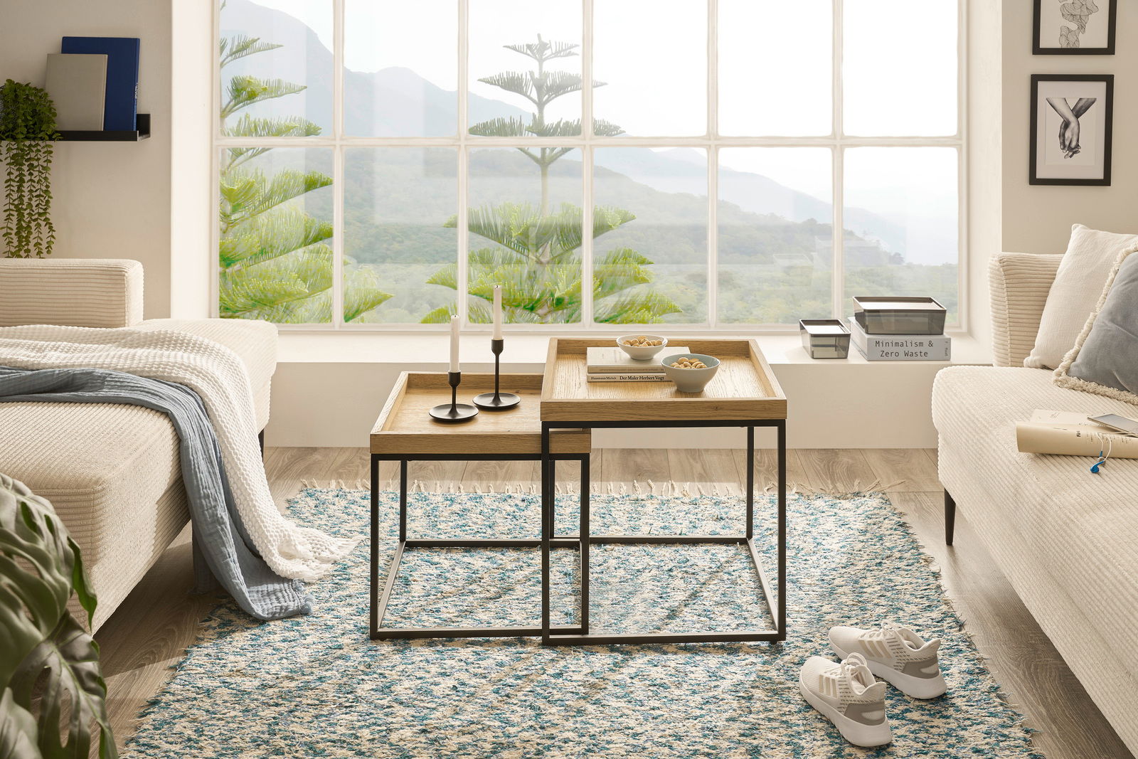 Zwei moderne Satztische aus Holz und Metall in einem gemütlichen Wohnzimmer mit Blick auf eine grüne Landschaft durch ein großes Fenster, von vorne betrachtet.