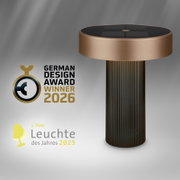 Moderne Tischleuchte mit zylindrischem, geriffeltem Fuß in Dunkelbronze und breitem, flachem Lampenschirm in Bronze mit dunkler Oberseite, freigestellt vor grauem Hintergrund; Ansicht schräg von vorne leicht von oben.