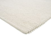 Nahaufnahme eines weißen Handwebteppichs aus Wolle, perspektivisch von der Seite aufgenommen.