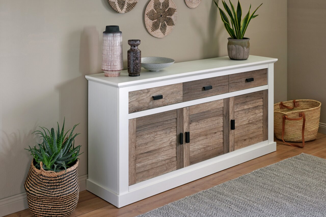Sideboard mit weißem Rahmen und Holztüren, dekoriert mit Pflanzen und Vasen, aus seitlicher Perspektive fotografiert.