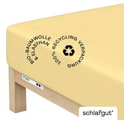 Gelbes Spannbettlaken aus Bio-Baumwolle und Elasthan auf einer Matratze, mit Recycling-Symbol, seitliche Perspektive