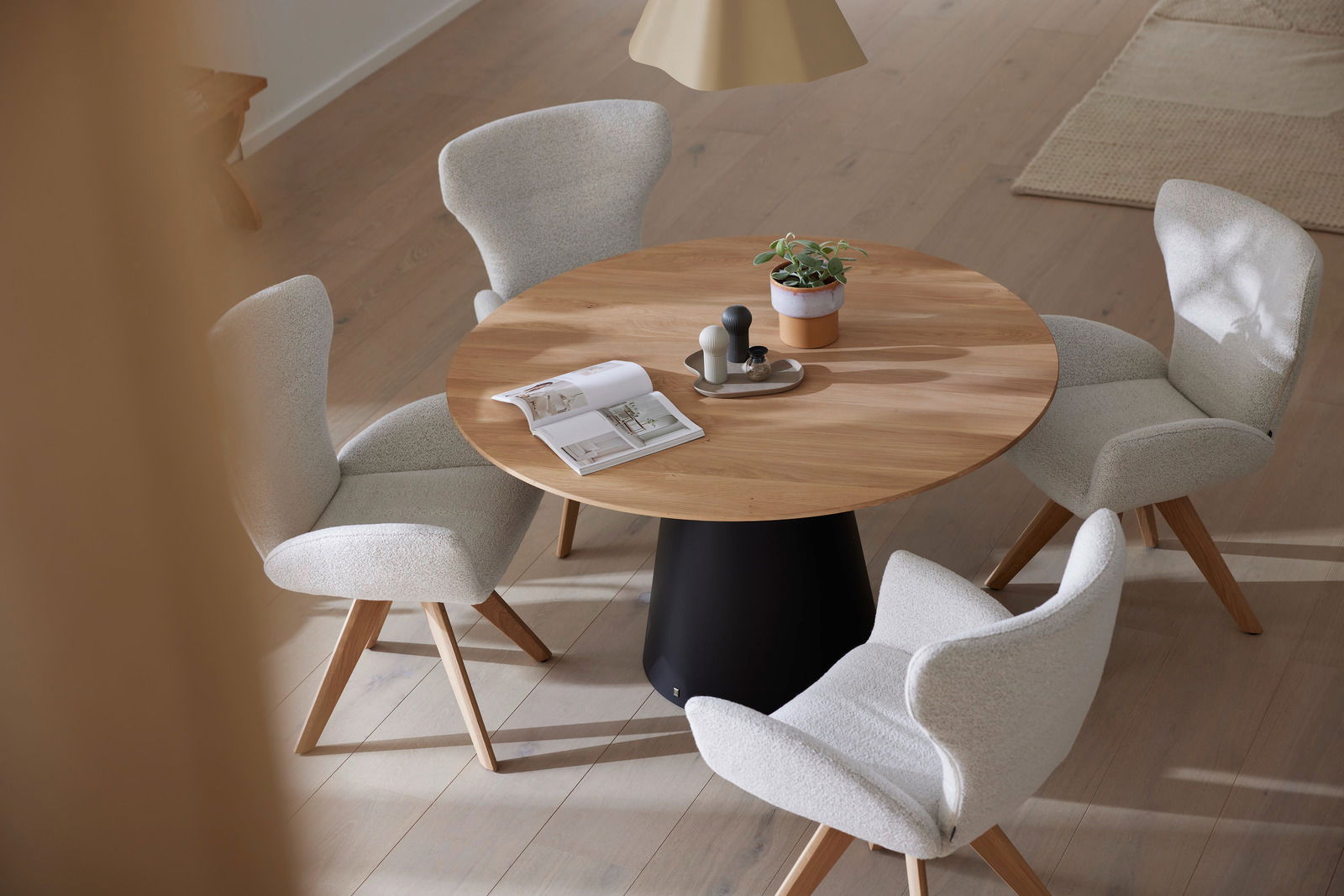 Runder Esstisch aus Holz mit schwarzem Sockel, umgeben von vier gepolsterten Armlehnstühlen in einem modernen Esszimmer. Perspektive von oben.