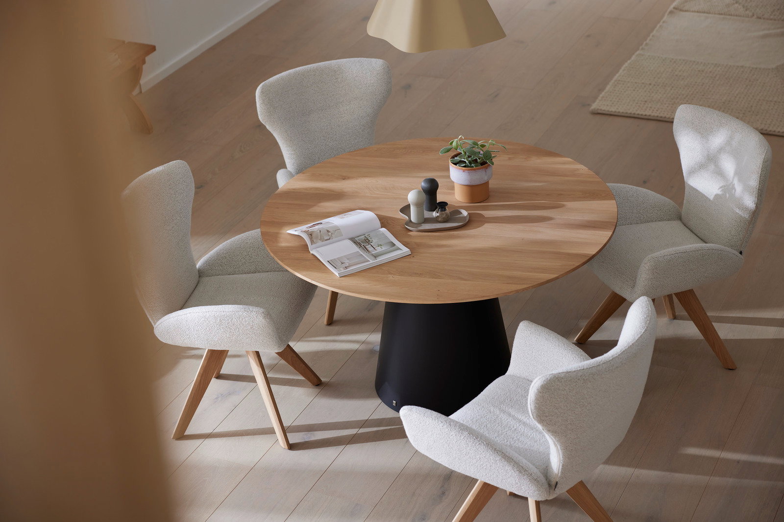 Runder Esstisch aus Holz mit schwarzem Sockel, umgeben von vier gepolsterten Armlehnstühlen in einem modernen Esszimmer. Perspektive von oben.