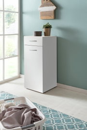 Witte wasmand met lade en deur, gezien vanaf de zijkant, versierd met een plant en een doos, tegen een mintgroene muur.